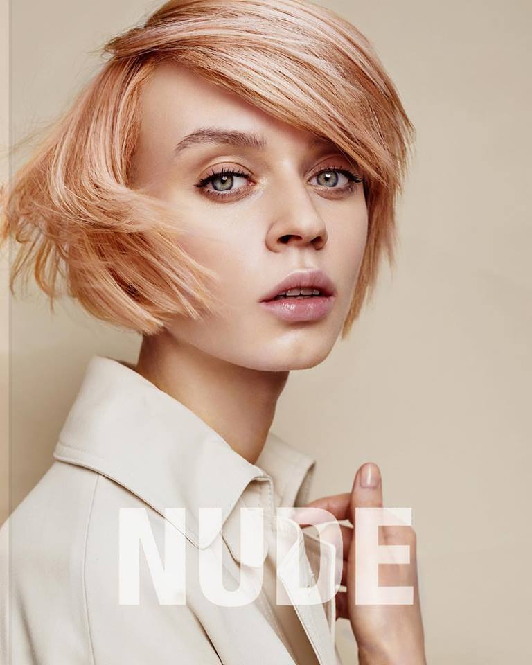 Mujer con cabello corto de color rosa claro, vestida con una chaqueta beige.