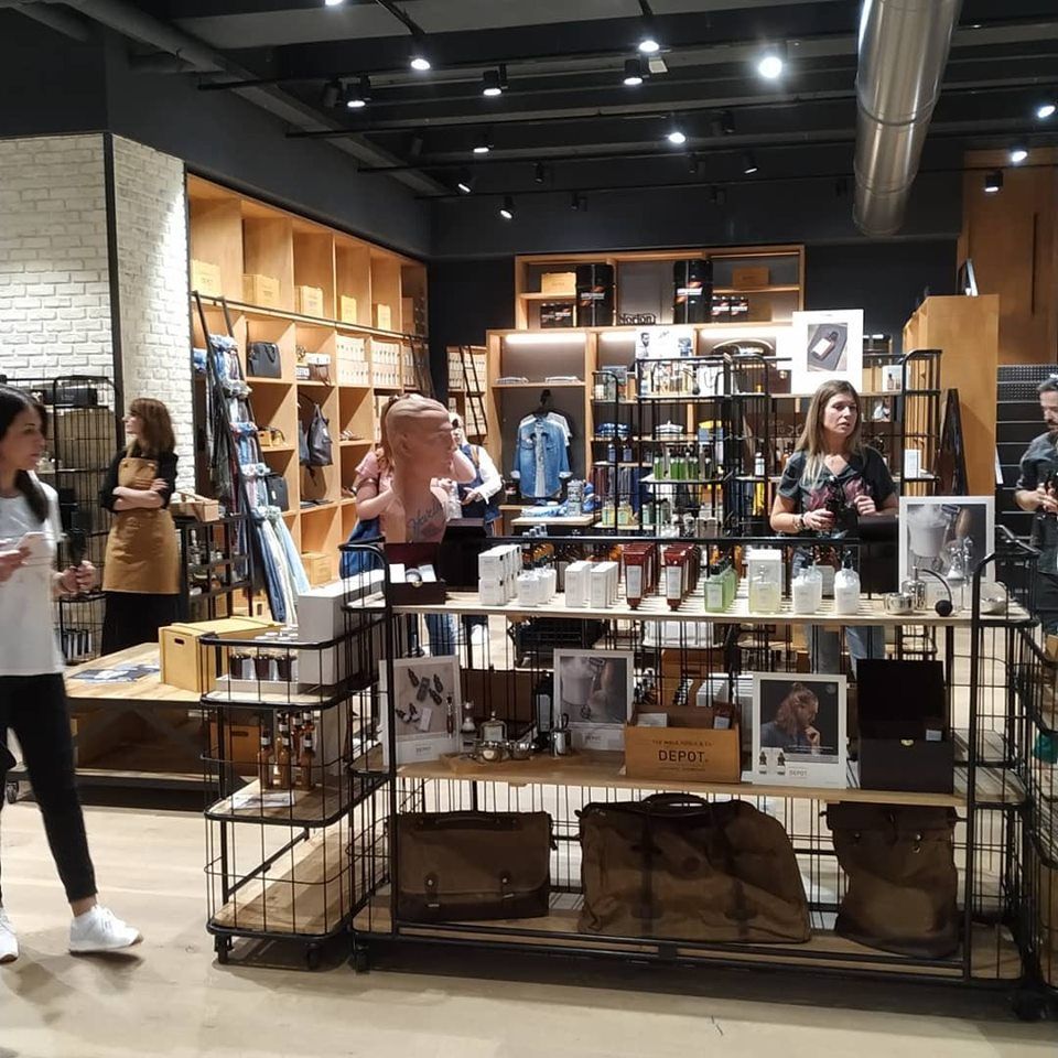 Dentro de una tienda, la gente mira los productos en exposición. Estantes de madera y estanterías metálicas en tonos neutros.
