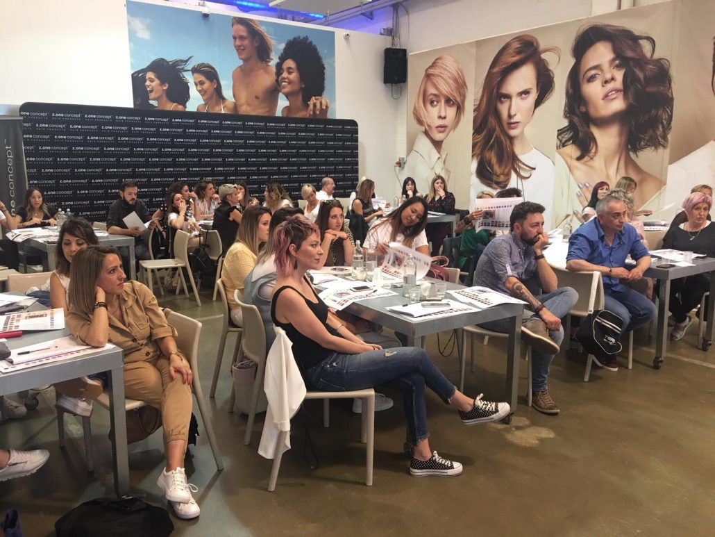 Público en un evento de capacitación de peluquería, sentados en mesas