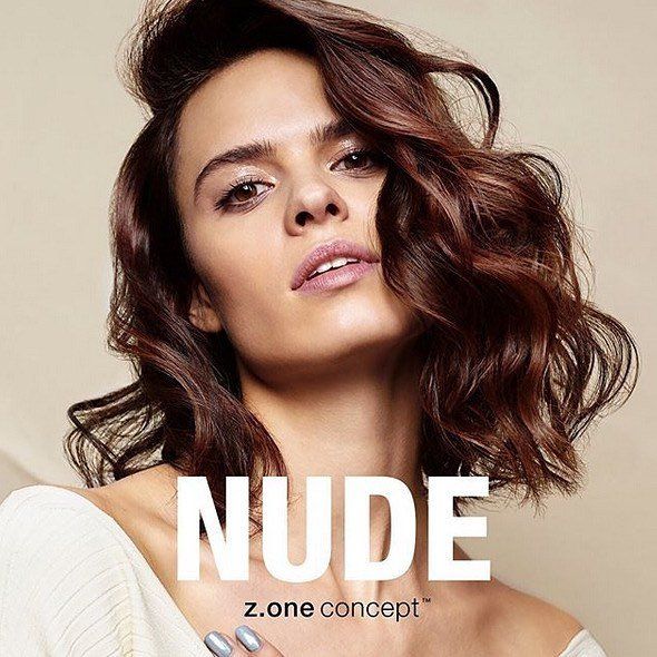 Mujer de cabello castaño ondulado, con maquillaje nude, bajo una luz tenue. El texto dice