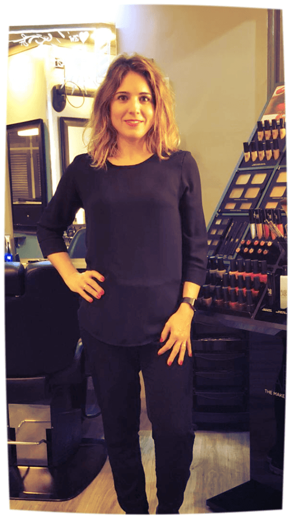 Mujer vestida de negro con la mano en la cadera, de pie en un estudio de maquillaje.