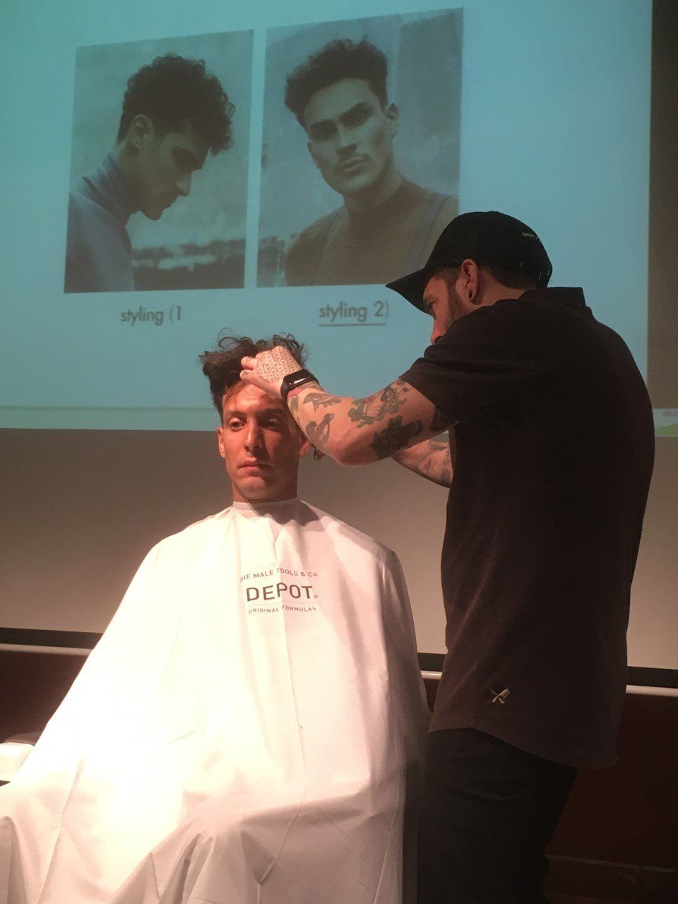Un barbero peinando el cabello de un hombre frente a una demostración proyectada.