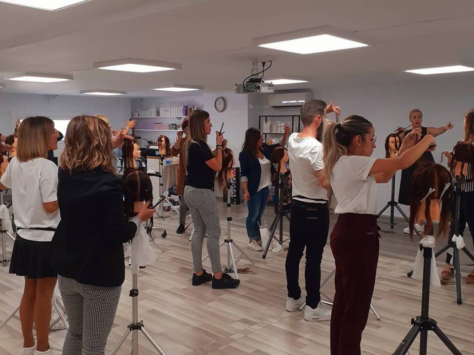 Los estudiantes de peluquería practican técnicas de corte en cabezas de maniquí en un aula luminosa.