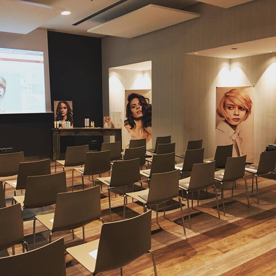 Sala de conferencias vacía con sillas frente a una pantalla y retratos de belleza.