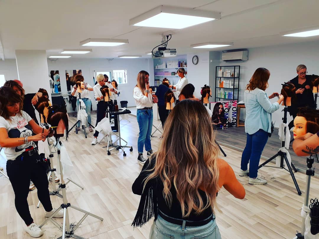 Los estudiantes de peluquería practican con maniquíes en un aula luminosa.
