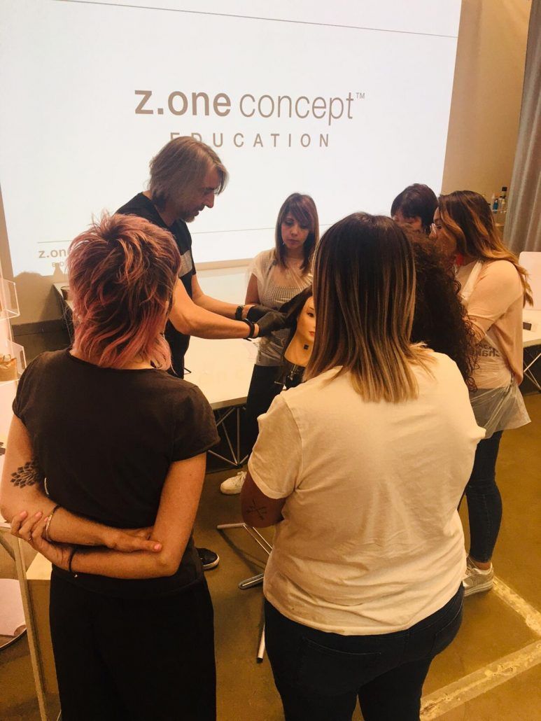 Clase de peinado con el instructor demostrando en un maniquí mientras los estudiantes observan.