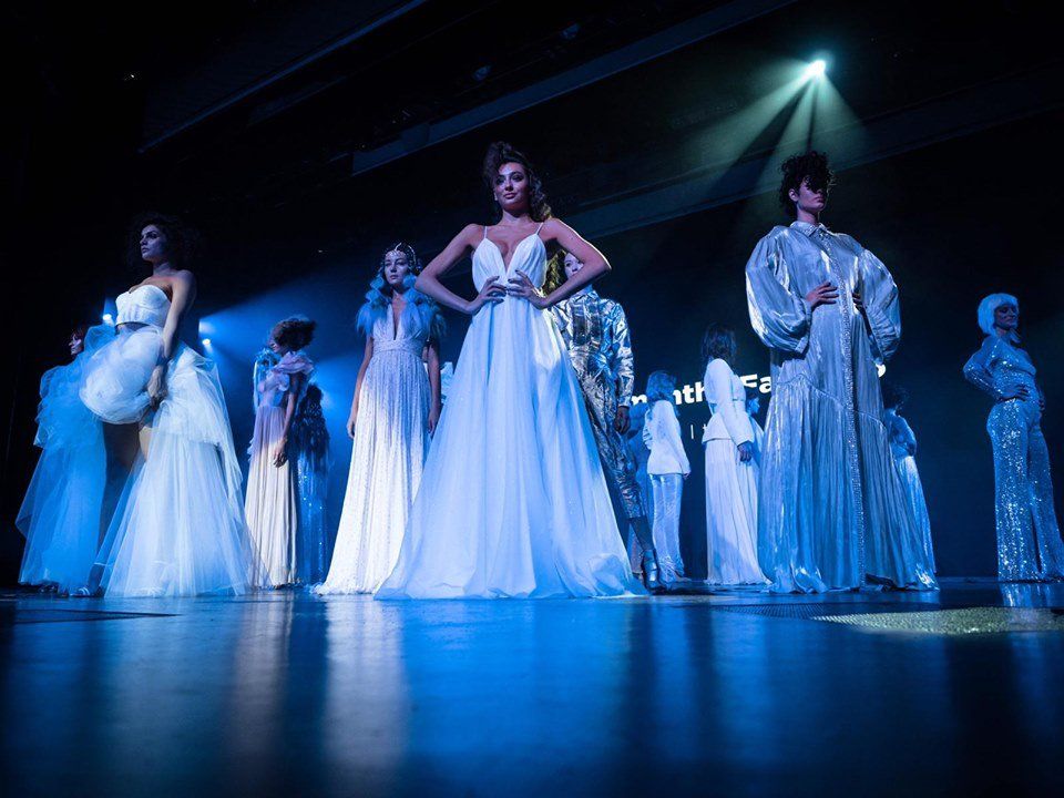 Modelos con elegantes vestidos blancos en una pasarela, iluminada por luces azules del escenario.