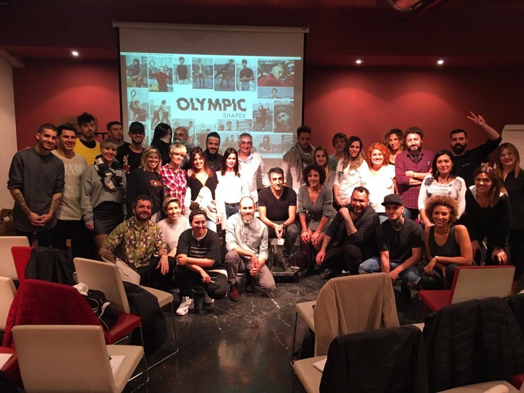 Un grupo grande posando en una sala con una pantalla que dice