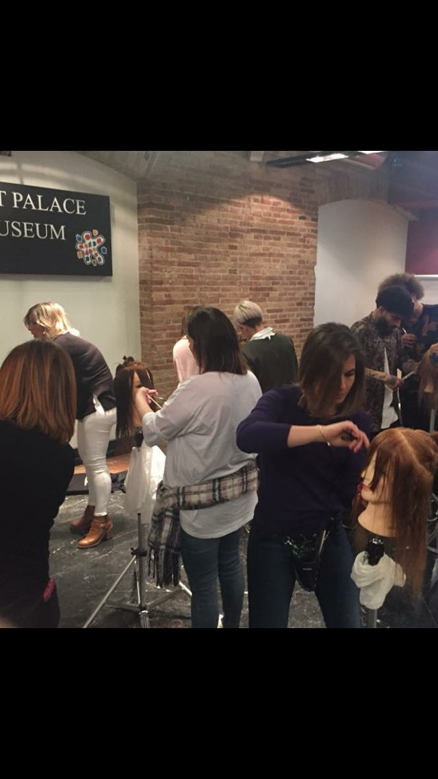 Personas asistiendo a una clase de peluquería en un espacio con paredes de ladrillo.
