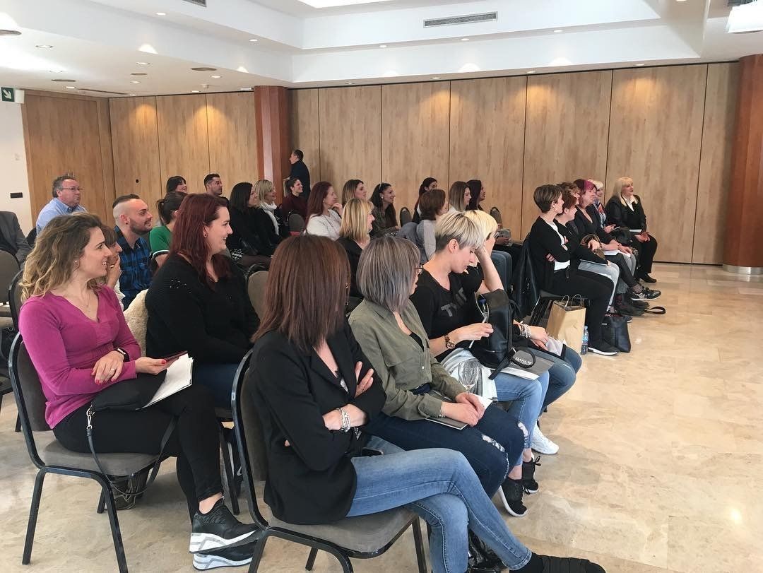 Personas sentadas, asistiendo a una conferencia o reunión en una sala con paneles de madera y paredes neutrales.