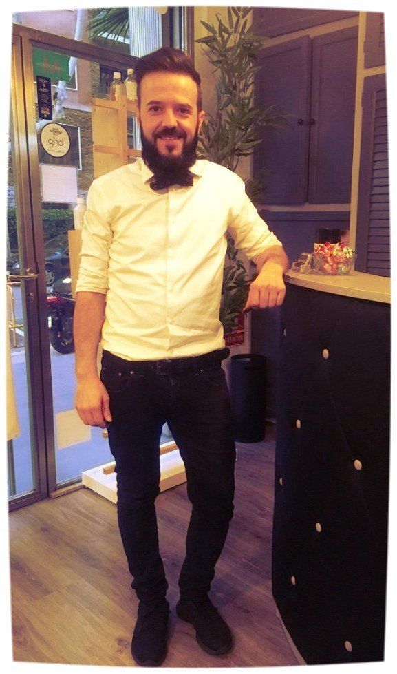 Hombre con barba, con pajarita y camisa blanca, apoyado en un mostrador negro.