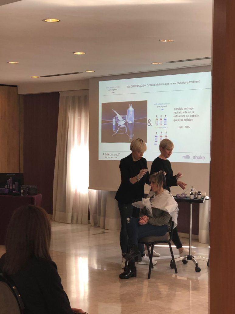 Dos estilistas muestran un corte de pelo a una persona sentada durante una presentación.