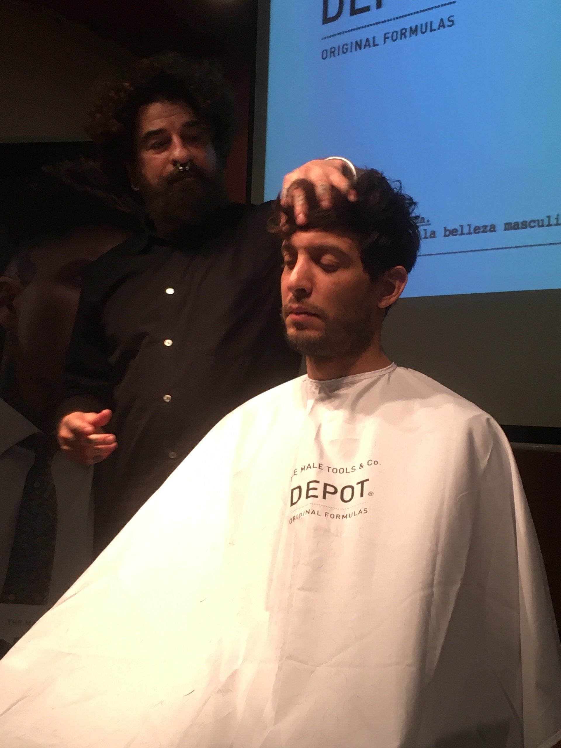 Un hombre se corta el pelo en una peluquería. Un barbero con barba le arregla el cabello oscuro a su cliente.