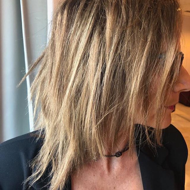 Mujer con cabello rubio despeinado y en capas, vestida con una chaqueta negra y gargantilla.