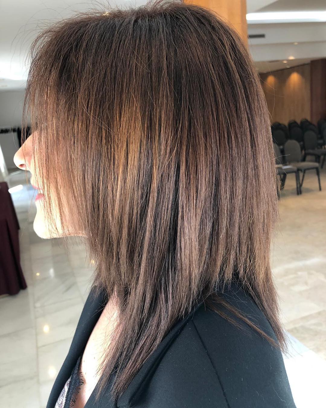 Mujer de cabello castaño oscuro y alisado con chaqueta negra. Interior.