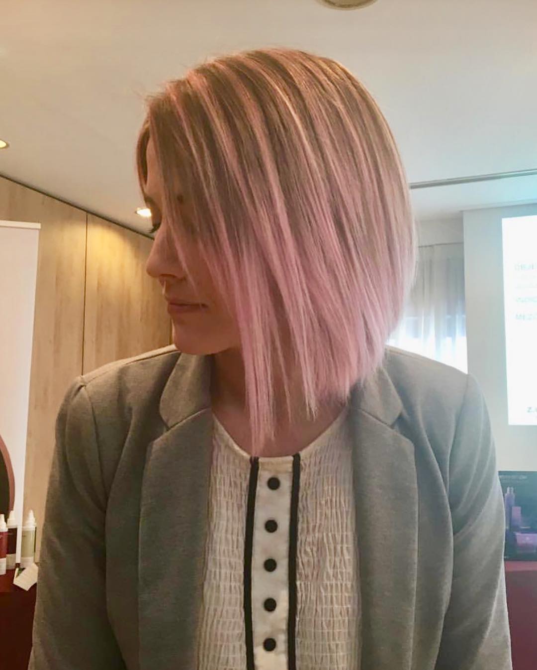 Mujer con un corte de pelo en ángulo y mechas rosas, vestida con un blazer gris