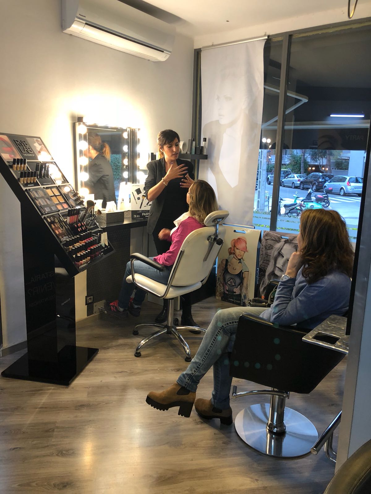 Una mujer en un estudio de maquillaje impartiendo una clase. Dos clientas sentadas, una de ellas maquillándose.