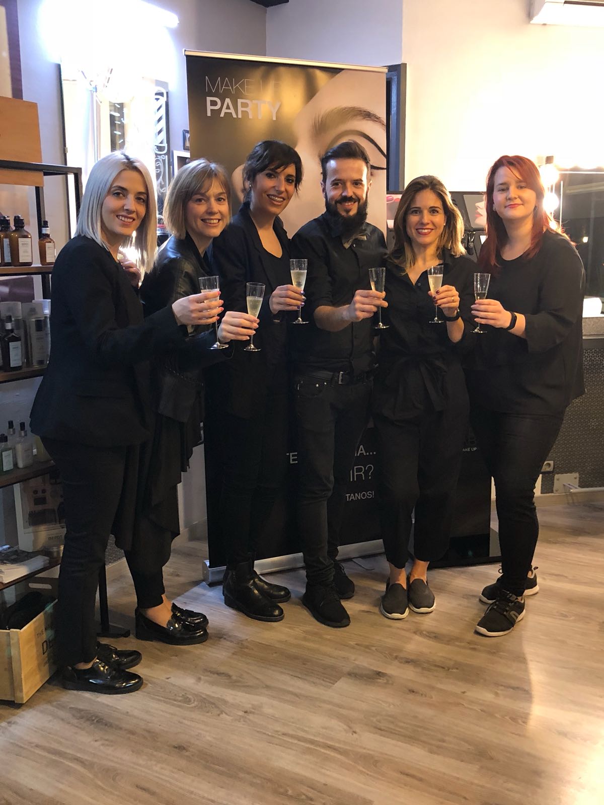 Seis personas vestidas de negro sosteniendo copas de champán, celebrando en una peluquería.
