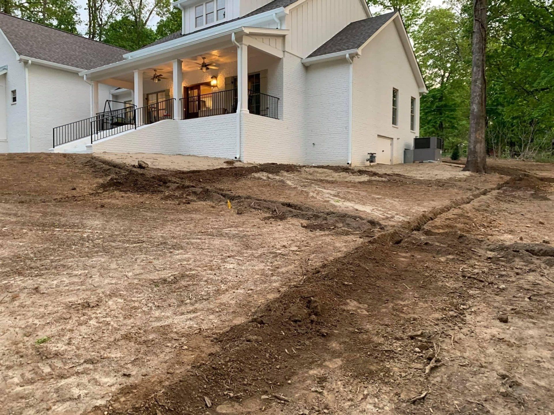 House under construction on a bare dirt lot with a partially visible porch and wooded background