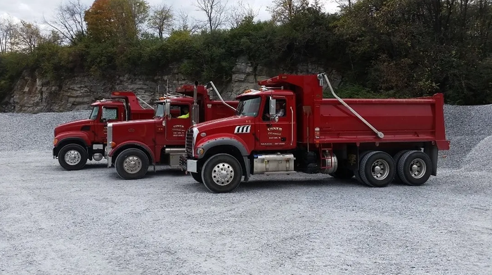 Grading Three red dump trucks are parked in a gravel lot.