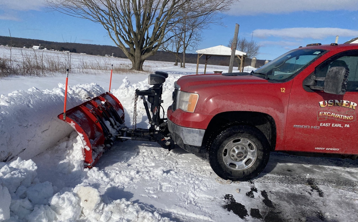 Additional Services A red truck with a snow plow attached to it is parked in the snow.
