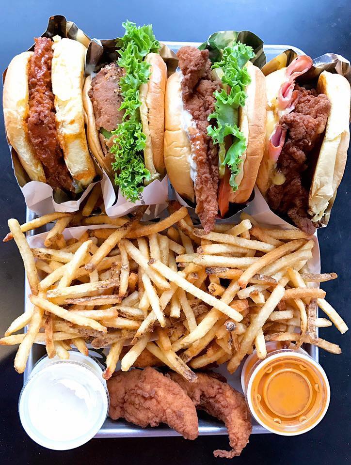 Fried chicken sandwiches, fries, sauces, and tenders on a tray.