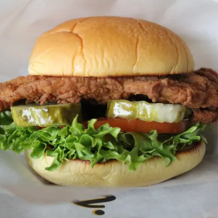 Fried chicken sandwich with lettuce, tomato, and pickles on a bun.