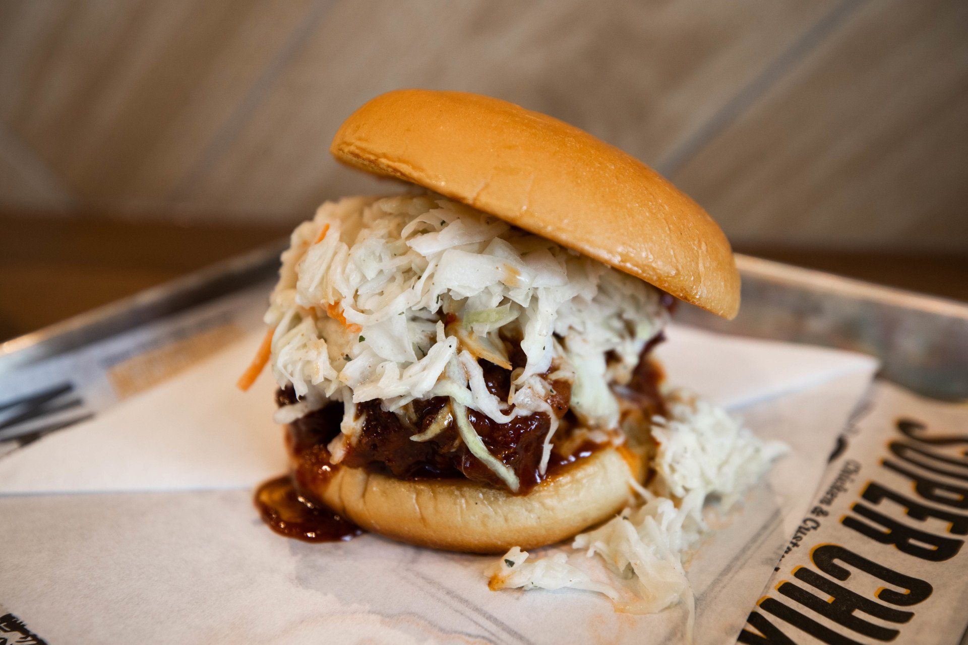 Pulled pork sandwich with coleslaw on a brioche bun, on paper, on a tray.