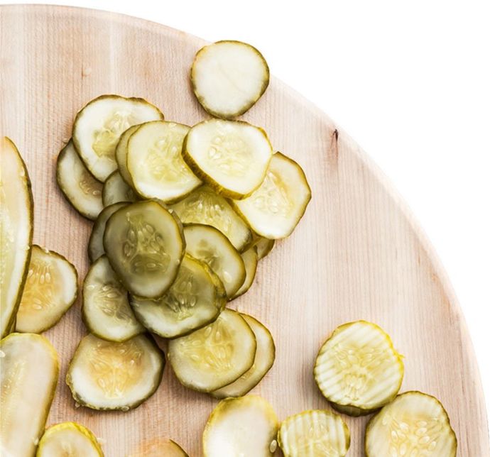 Sliced pickles on a wooden cutting board, overhead view.