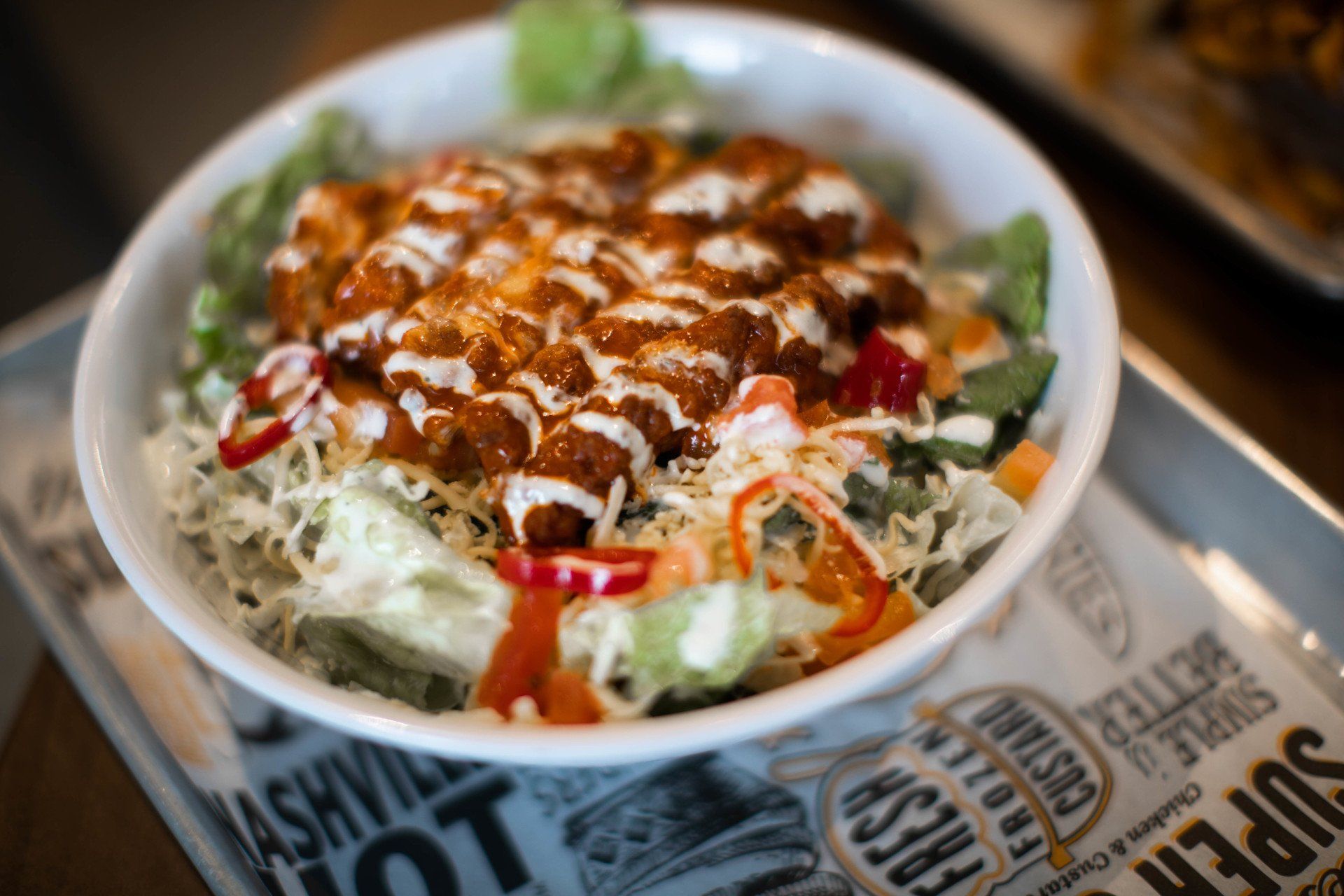 Salad bowl with fried chicken, lettuce, vegetables, and creamy dressing.