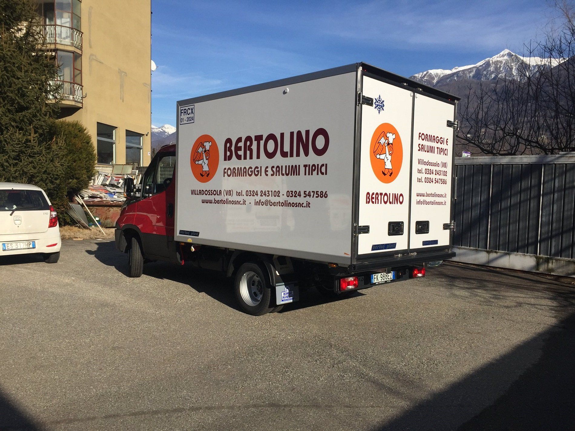 Un camion commerciale bianco parcheggiato su un piazzale ghiaioso con le montagne sullo sfondo, recante il marchio