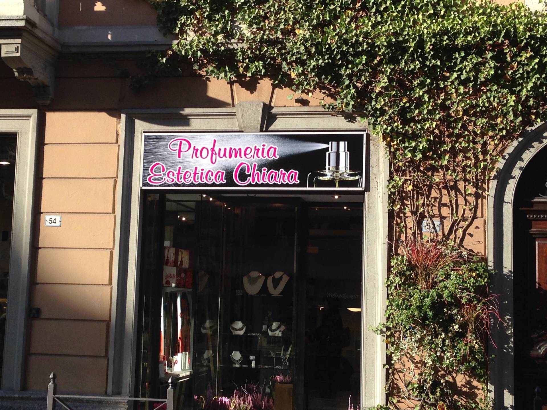 La vetrina di un negozio a Roma per Profumeria Estetica Chiara, con insegna rosa ed edera rampicante sulla facciata.