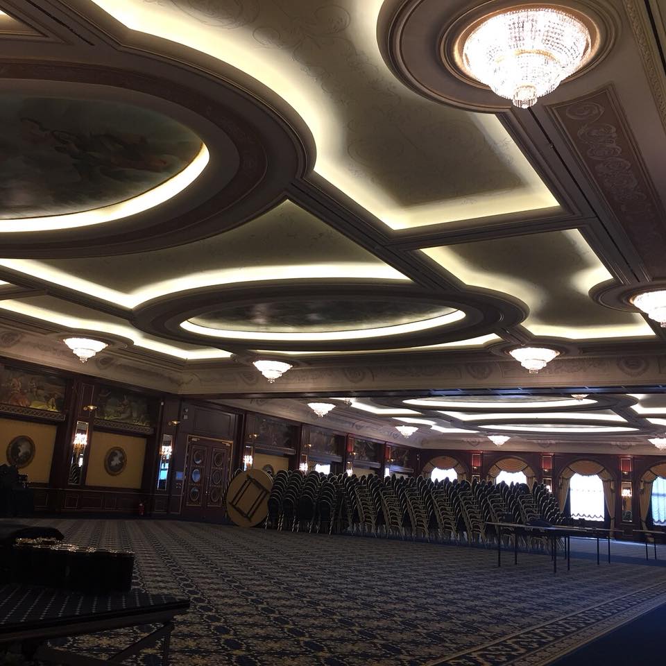 L'elegante sala da ballo di un hotel presenta una moquette decorata, modanature a più livelli sul soffitto con illuminazione integrata e lampadari.