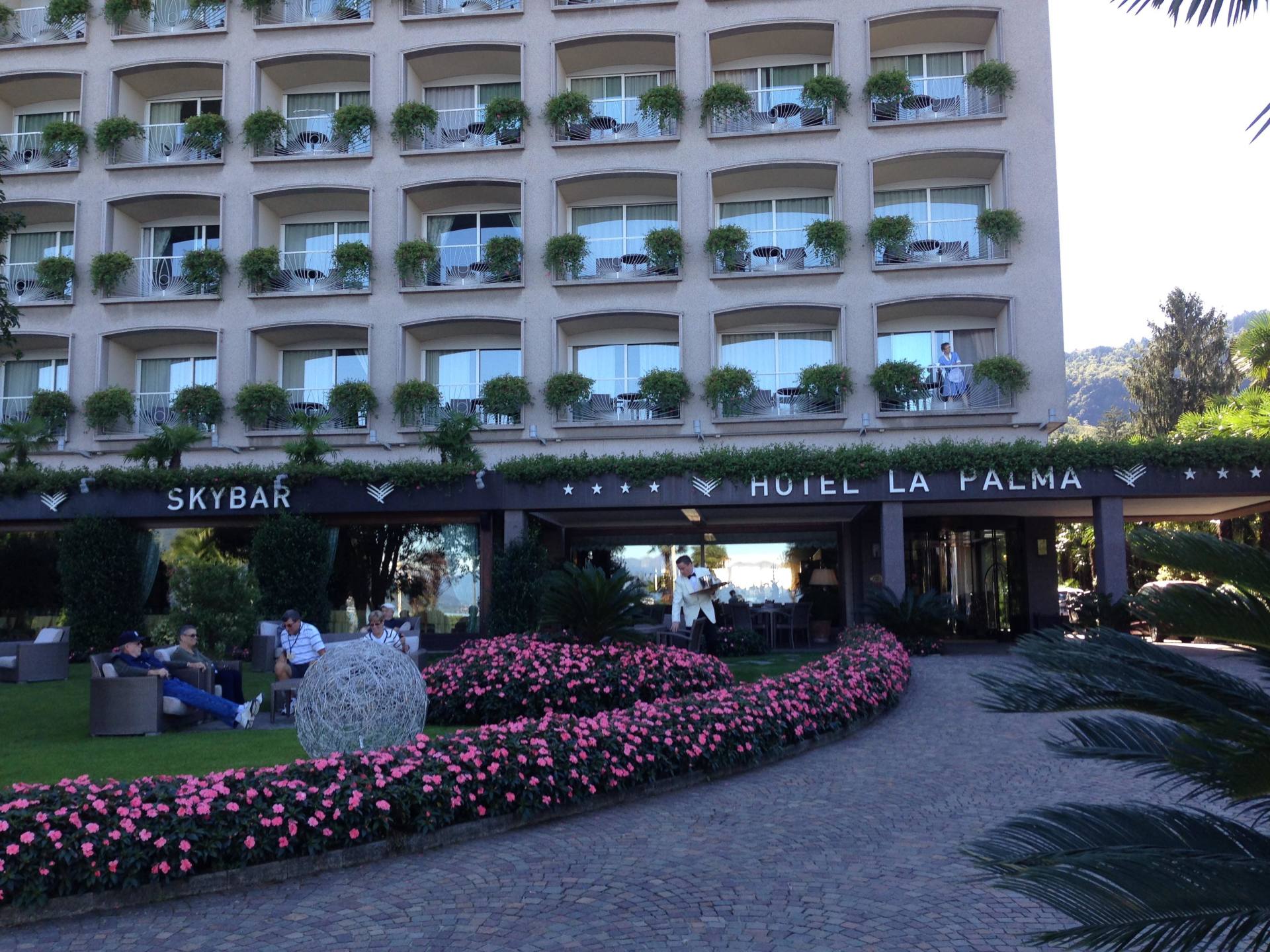 L'ingresso dell'hotel si compone di un edificio di cinque piani, uno Skybar al piano terra e un giardino con fiori rosa e area salotto.