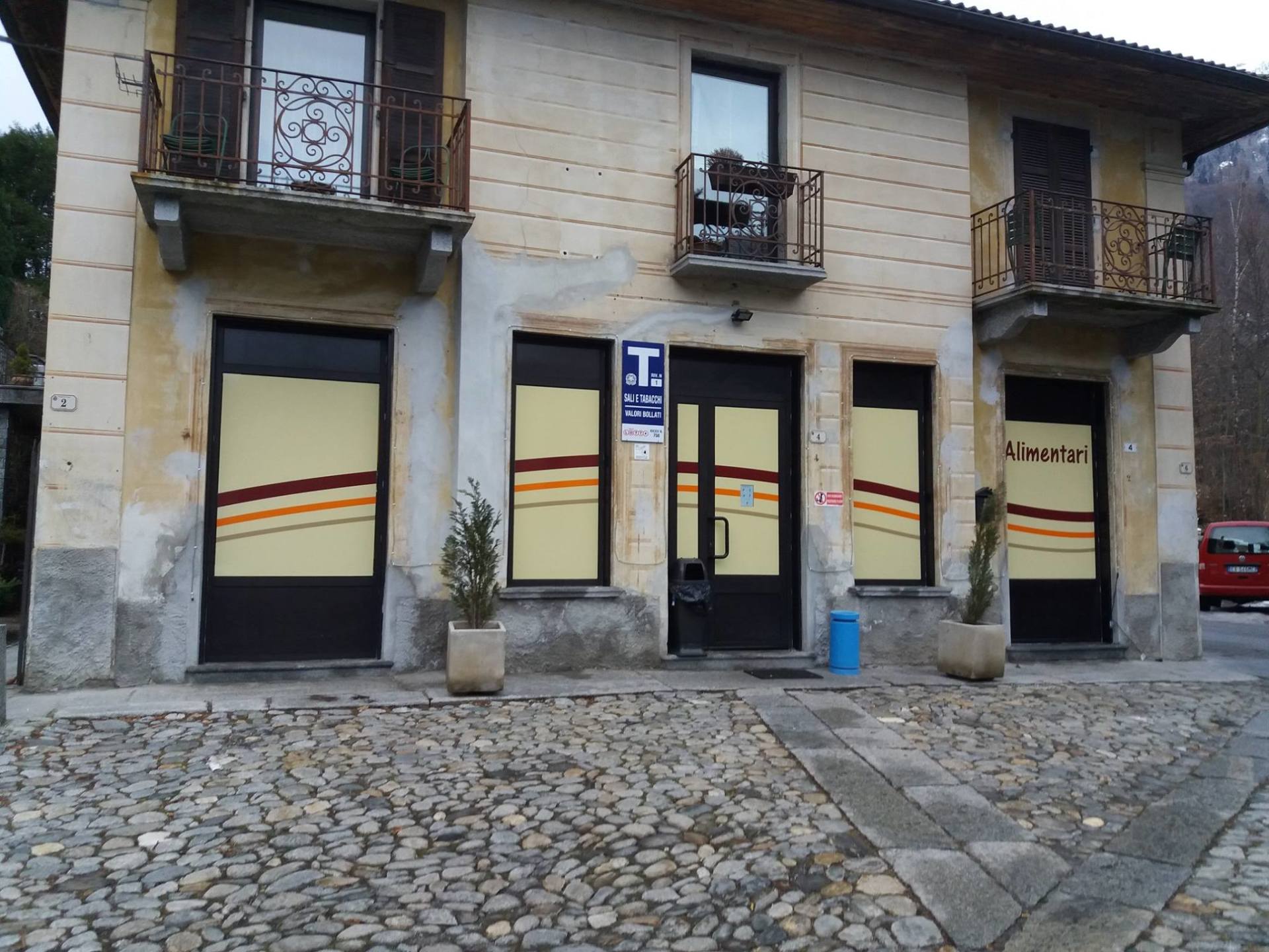 Un edificio a due piani con strada lastricata, muri beige, balconi in ferro battuto e vetrine con strisce marroni.