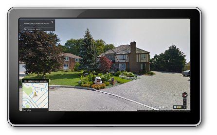 Tablet displaying a Google Street View of a large house with a gravel driveway, trees, and a map in the corner.