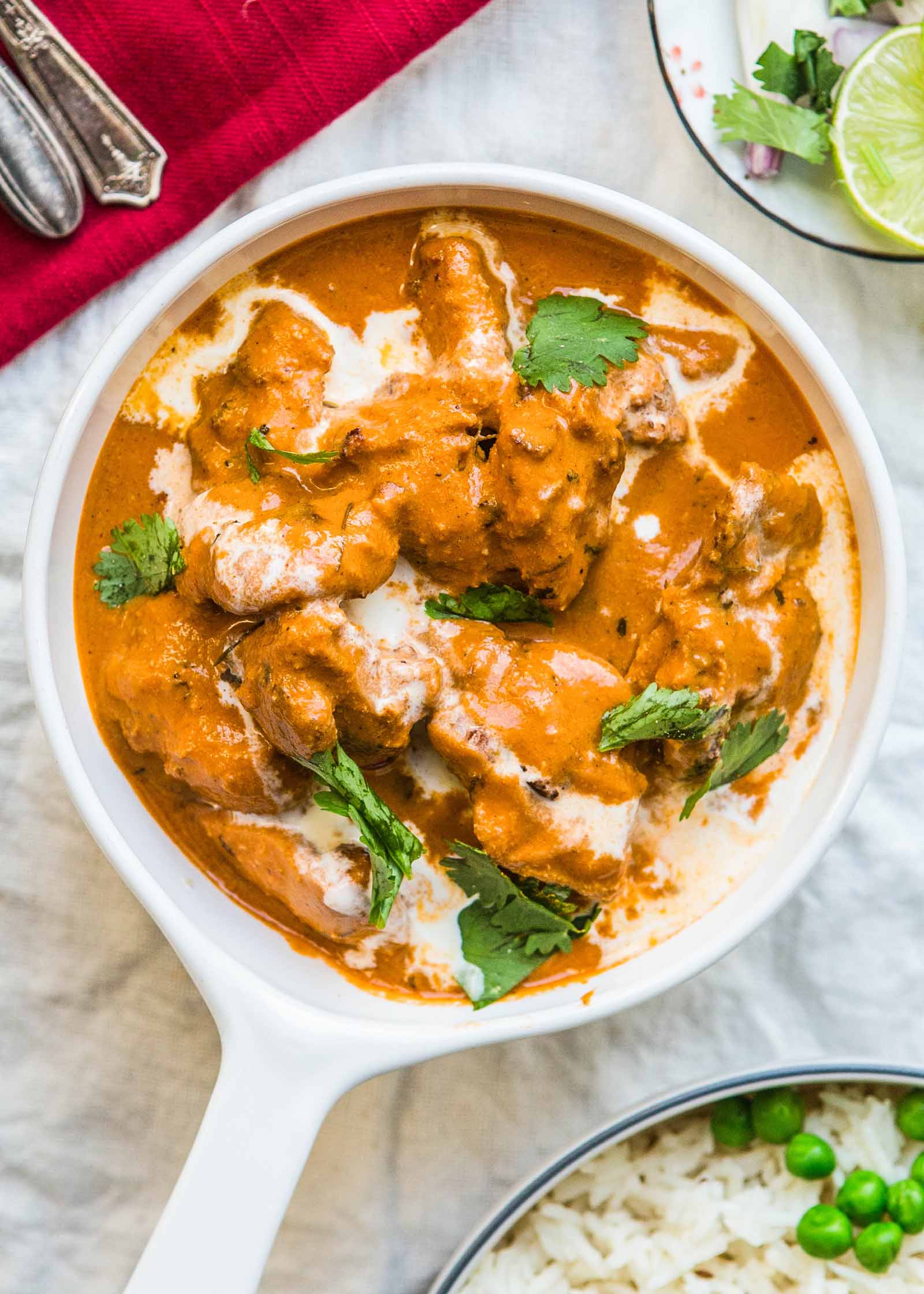 A bowl of chicken tikka masala with rice and peas on a table.