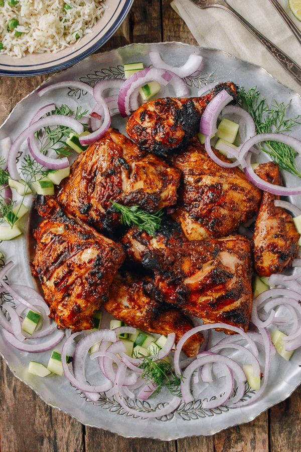 A plate of grilled chicken with onions and cucumbers on a wooden table.