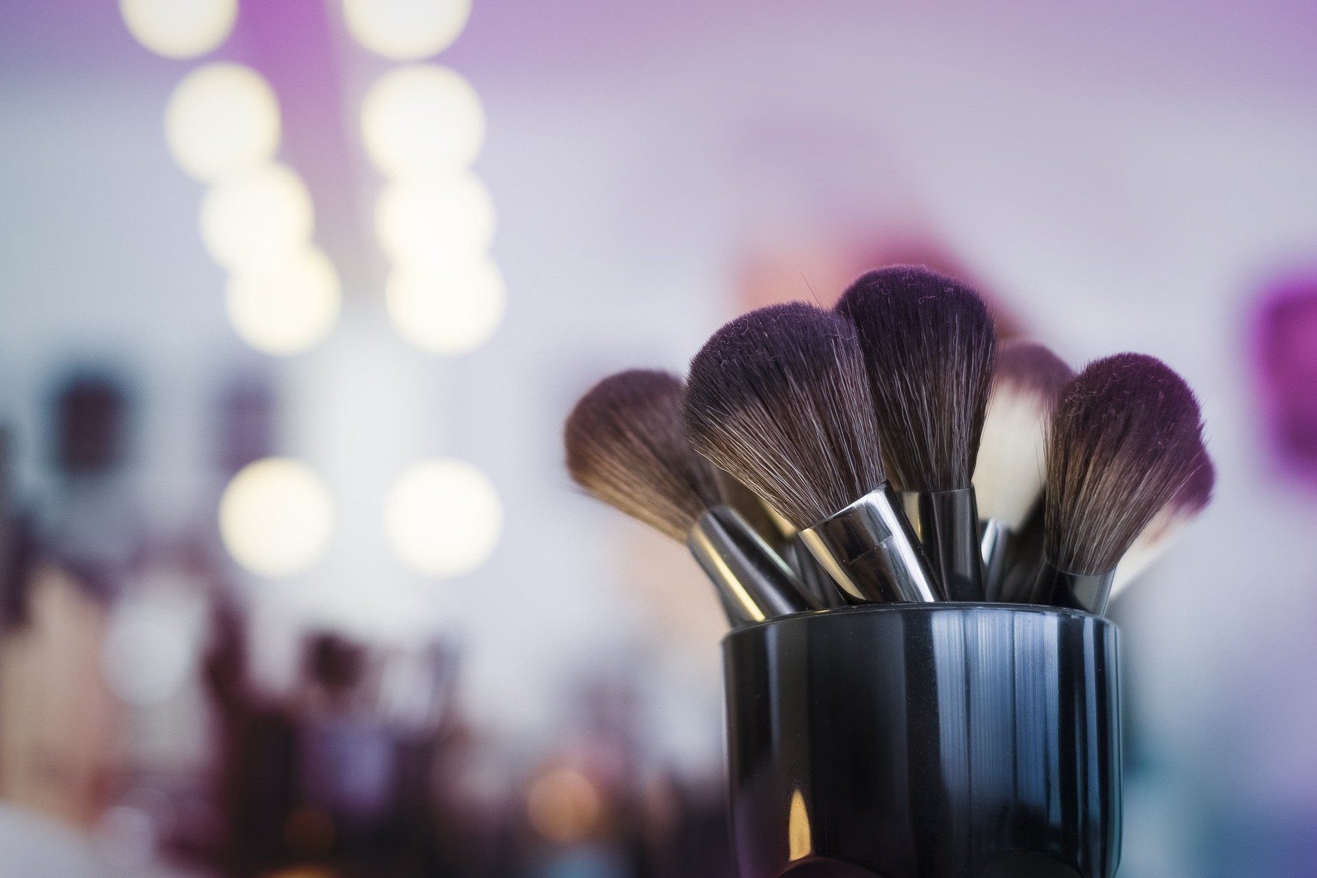 A bunch of makeup brushes in a black cup on a table.