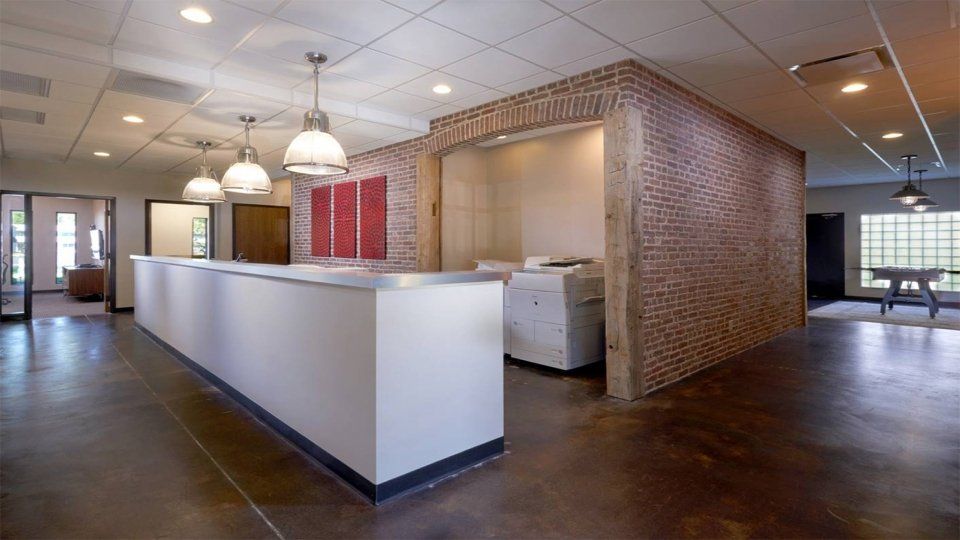 Huge reception table in a wide office space that consist of three big lamps placed on the ceiling and white photocopying machines inside.