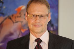 Mann mit Brille und Anzug, lächelnd, vor abstrakter Kunst.