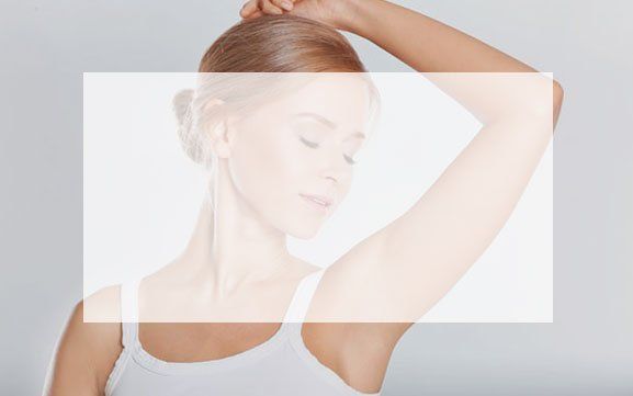 A woman in a white tank top is holding her hair in a bun.