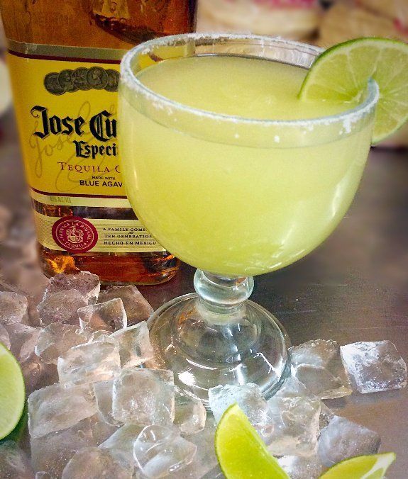 Margarita in a salt-rimmed glass with lime, bottle of Jose Cuervo tequila, and ice cubes.