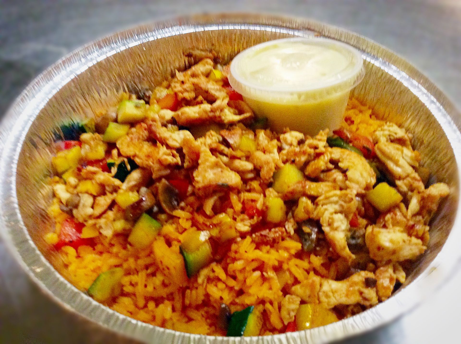 Chicken and rice bowl with vegetables and sauce in a foil container.
