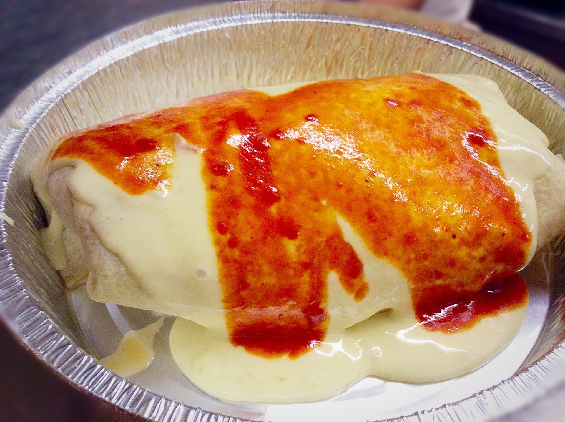 Burrito covered in cheese sauce and red sauce in a foil container.