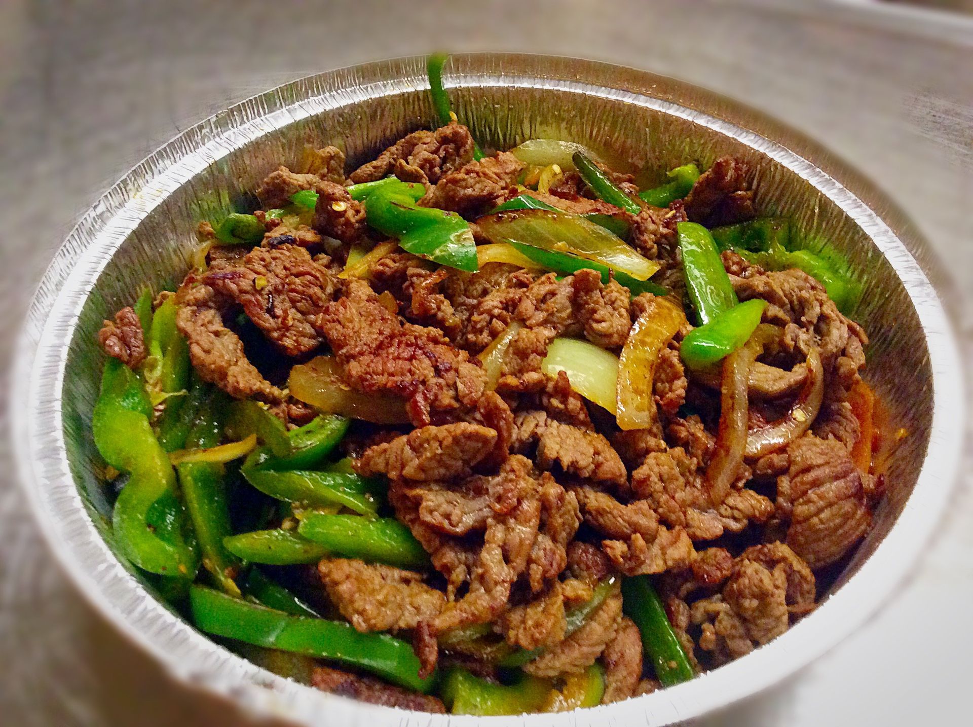 Beef and green peppers stir-fry in a silver foil container.
