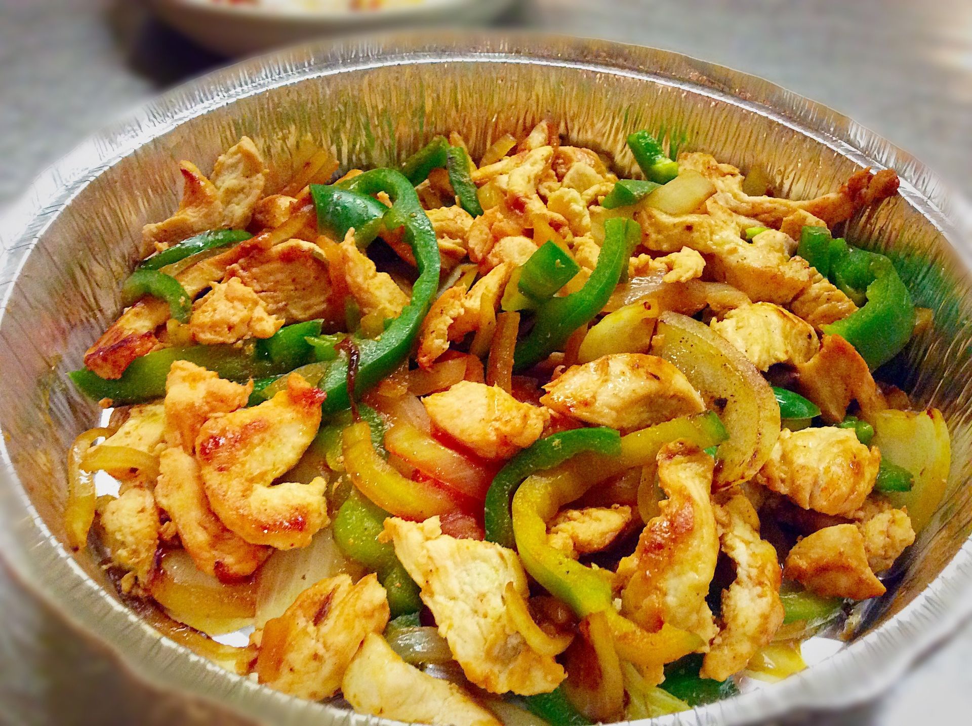 Chicken fajitas with green peppers and onions in a foil container.
