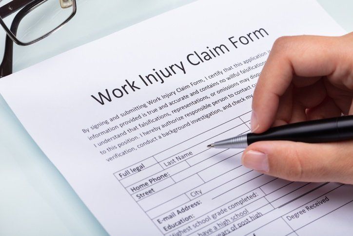 Divorce Attorney — Work Injuries in Union City, TN Person filling out a work injury claim form with a pen. Glasses are on the side.