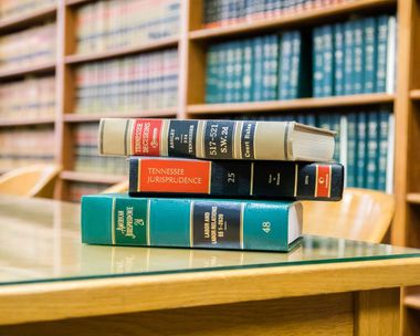 Books stacked on a table in a library. Shelves of books in the background.