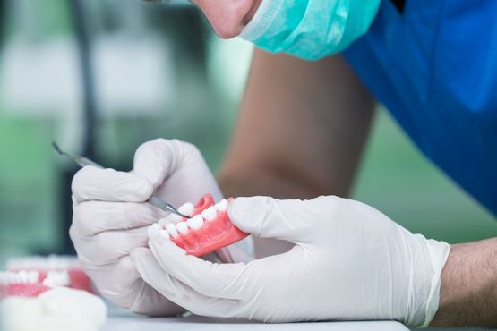 Dentist in gloves working on dentures, using a tool.